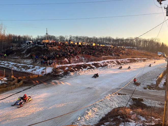 Snowmobiles race around the I-500 track before a large crowd.