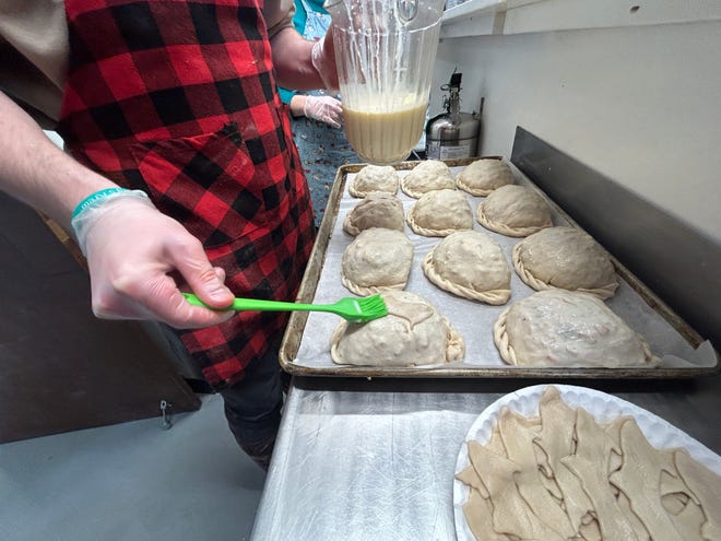 A baker brushes egg wash onto a tray of pasties.