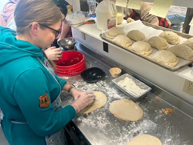 A baker rolls pasty dough on a floured work surface.
